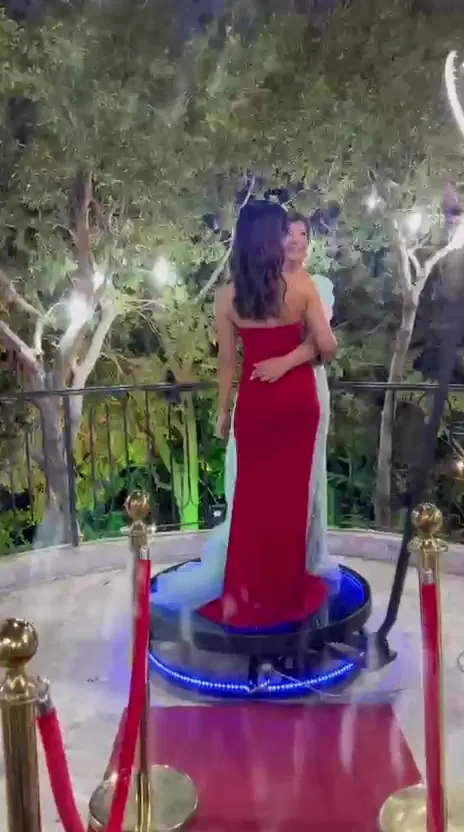 A guest in a red gown standing on the 360 cam platform under the ring light