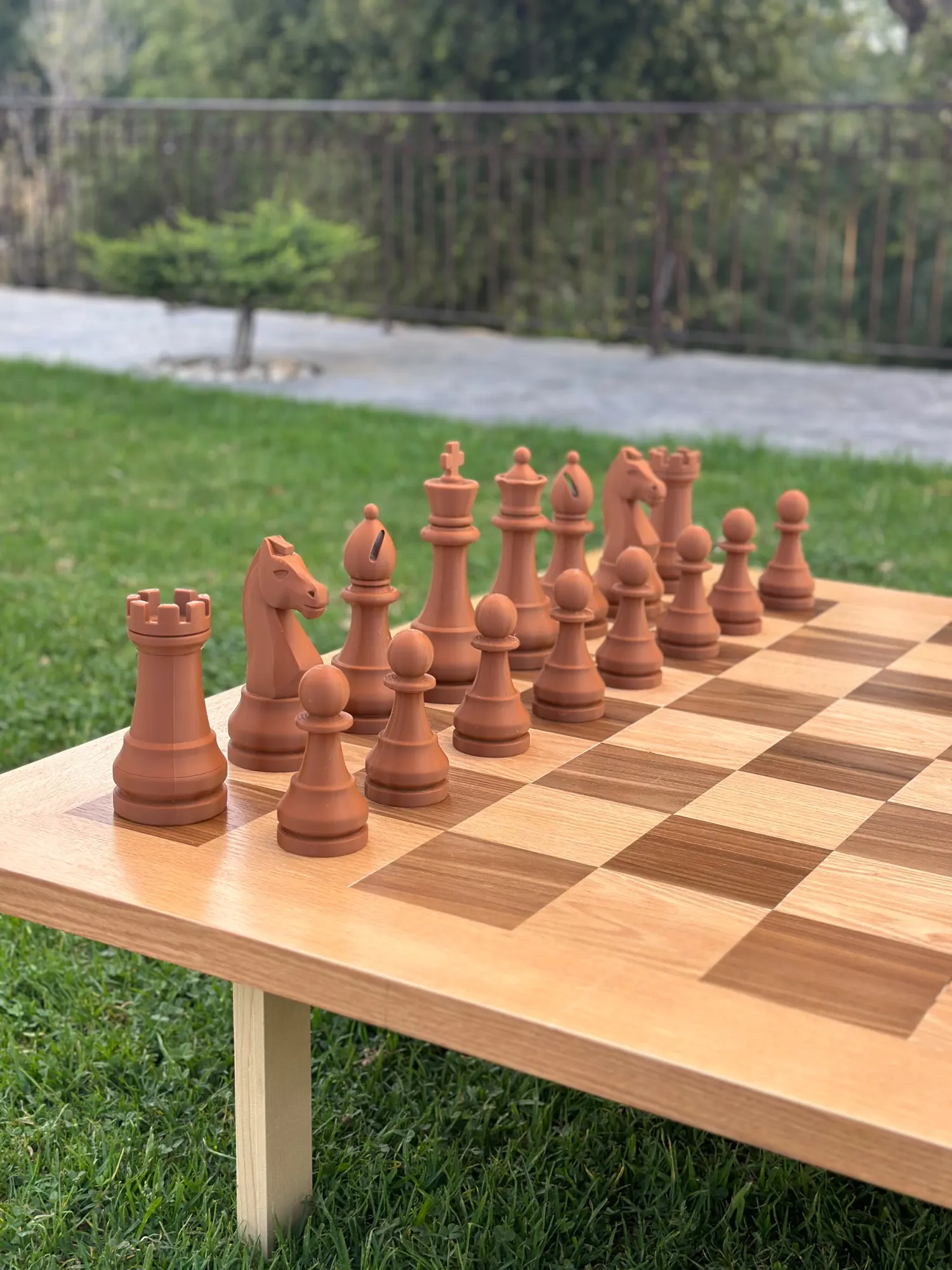 A giant chess set with terracotta pieces on a lawn