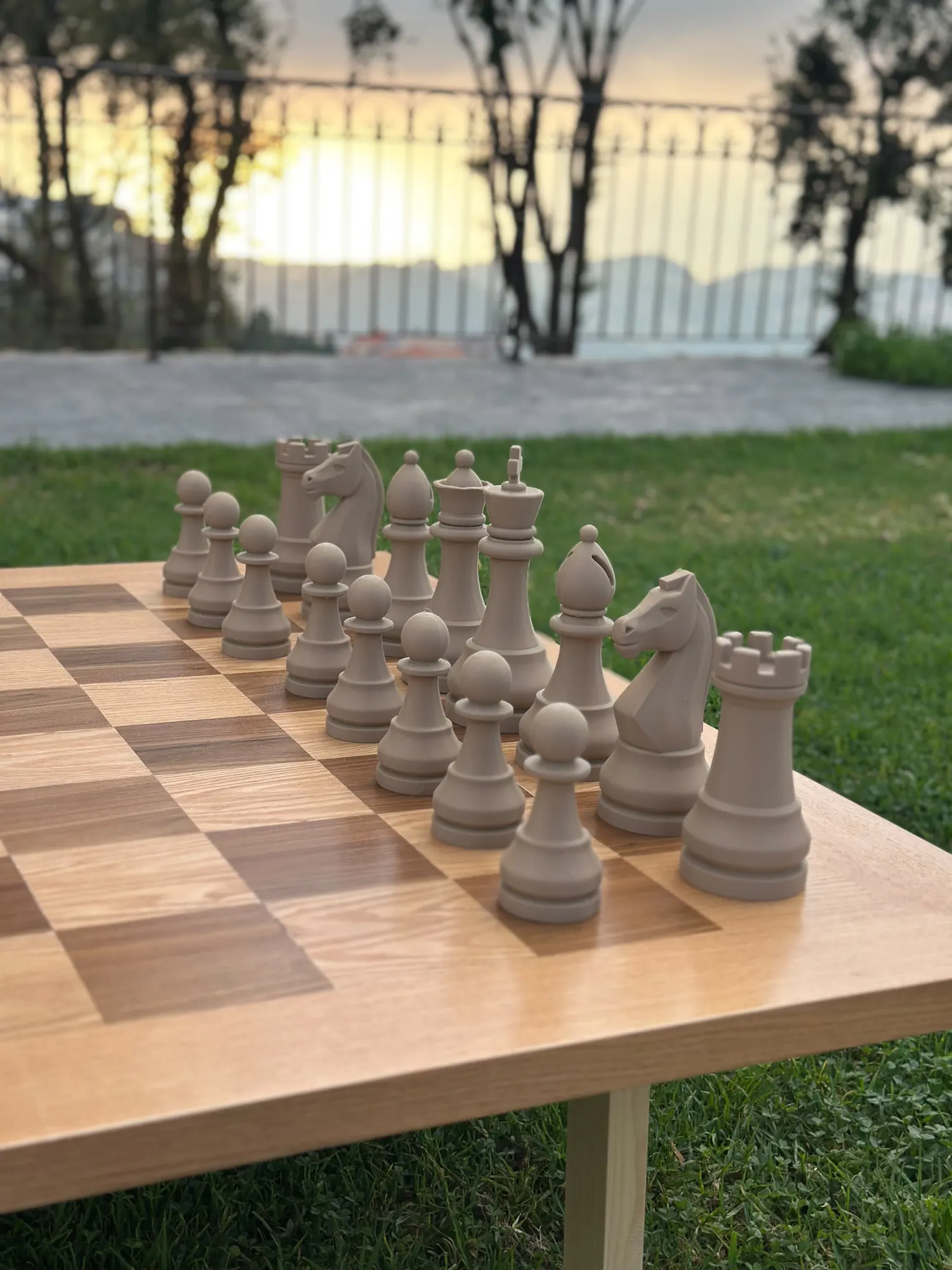 A giant chess set on a lawn with the sun going down behind the trees