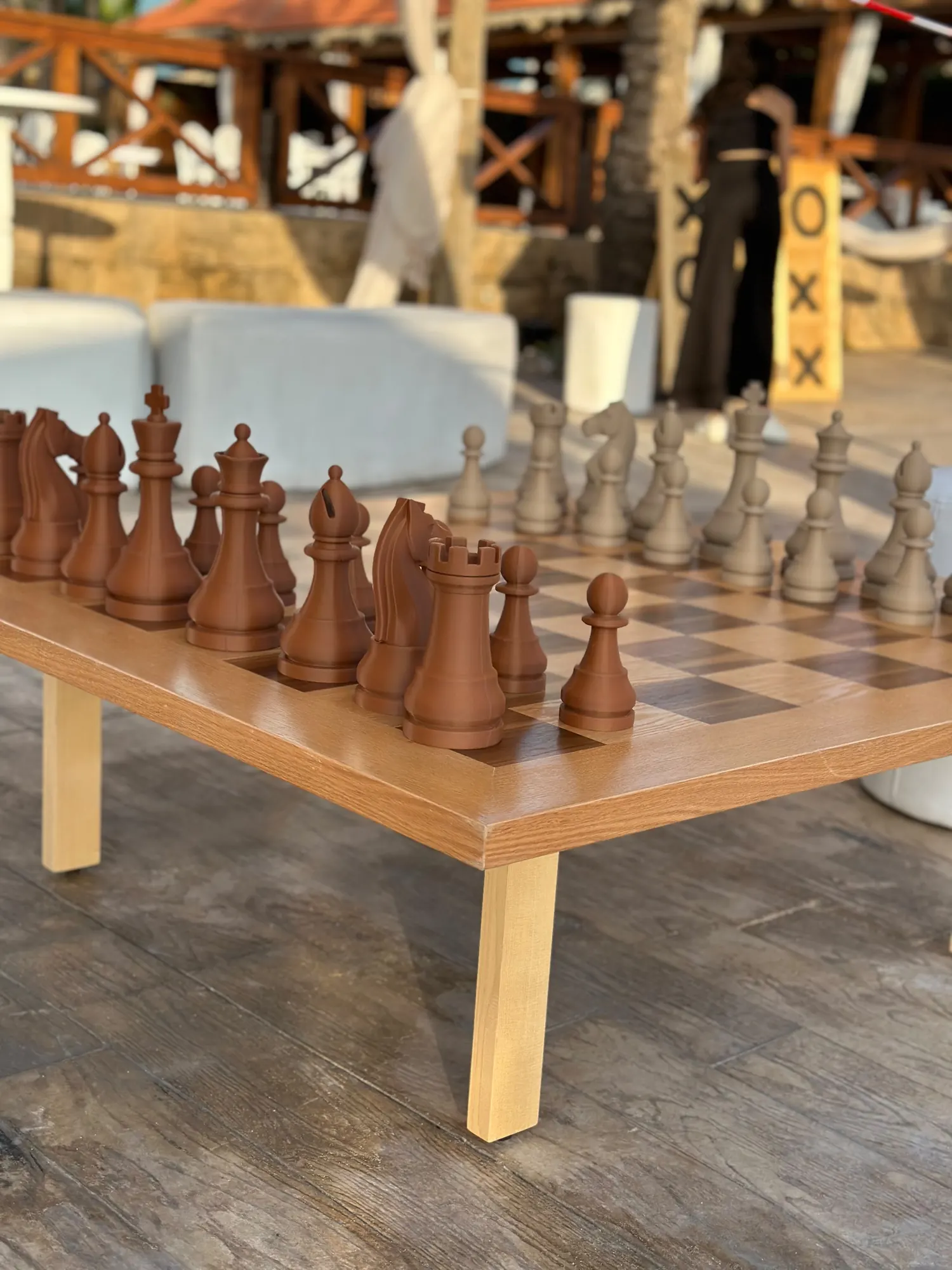 A giant chess set on a wooden terrace beside lounge seating