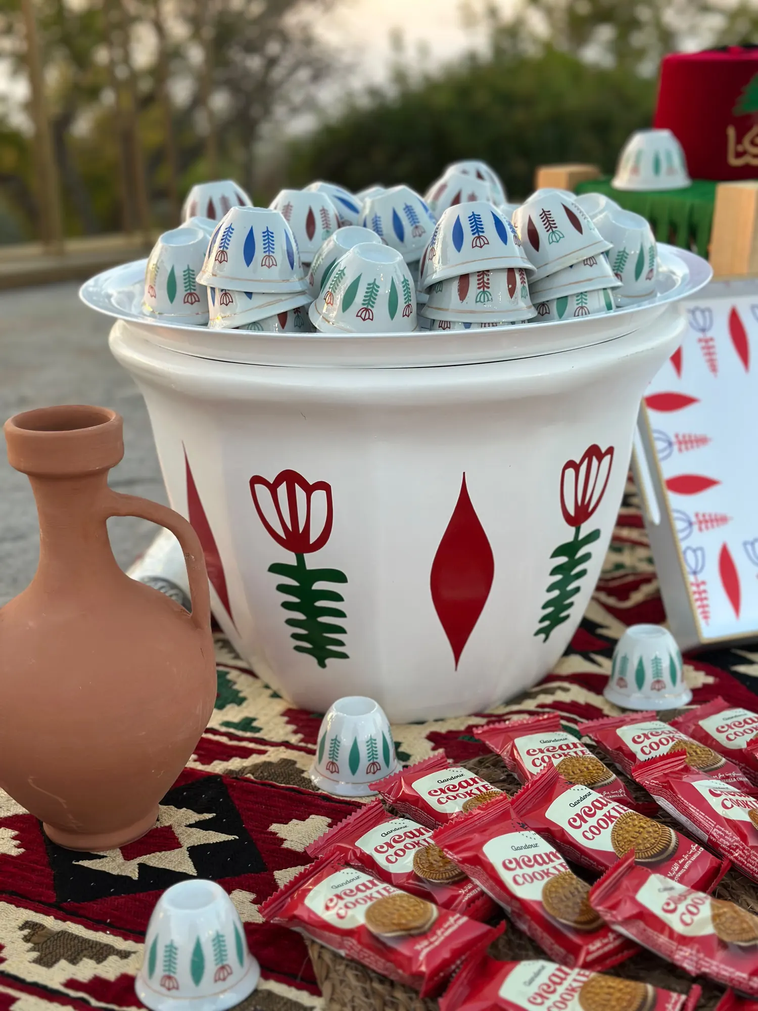 Arabic coffee cups stacked in a painted bowl beside a clay jug