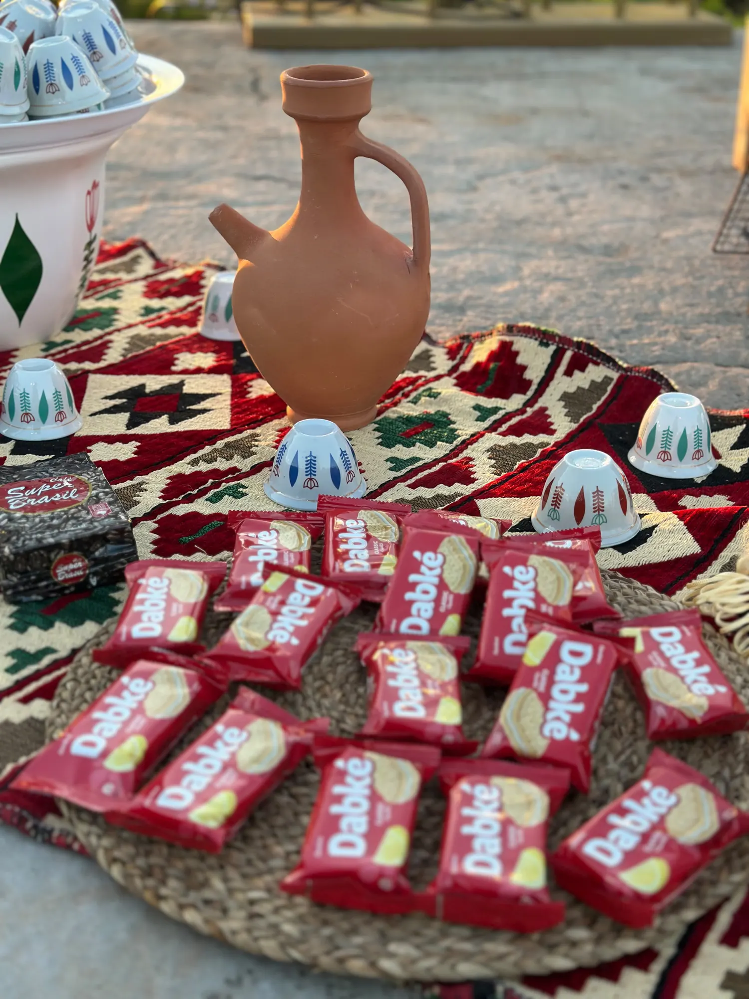 A clay jug surrounded by wrapped biscuits on a woven mat