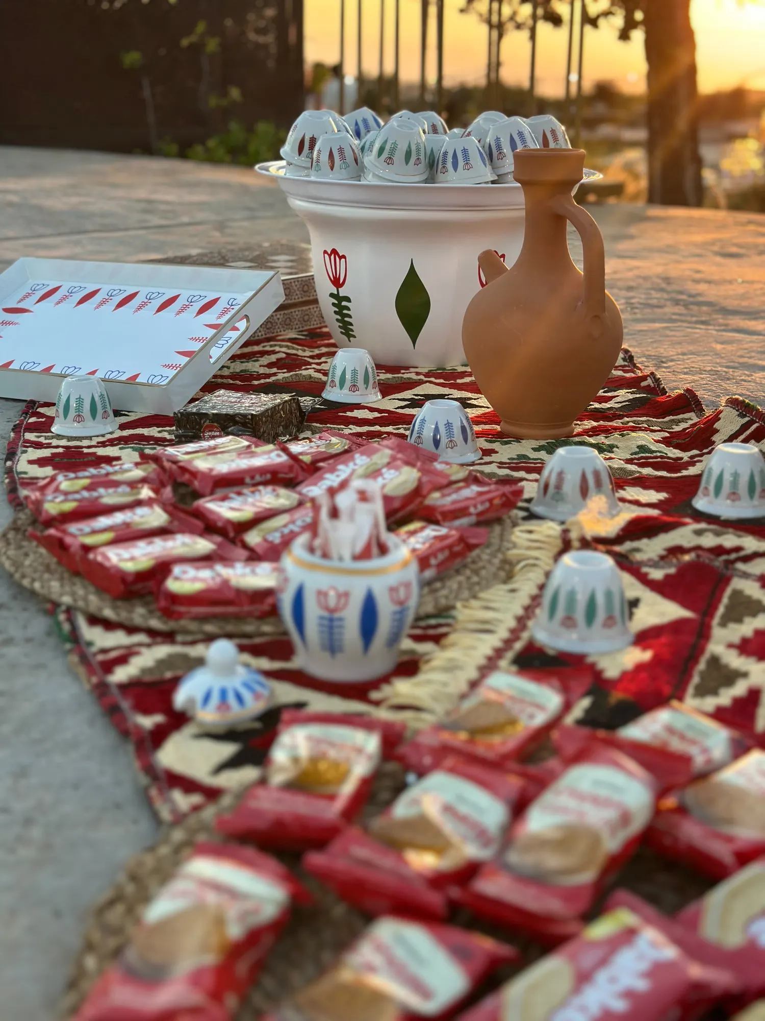A full Arabic coffee and biscuit spread laid out on a kilim at sunset