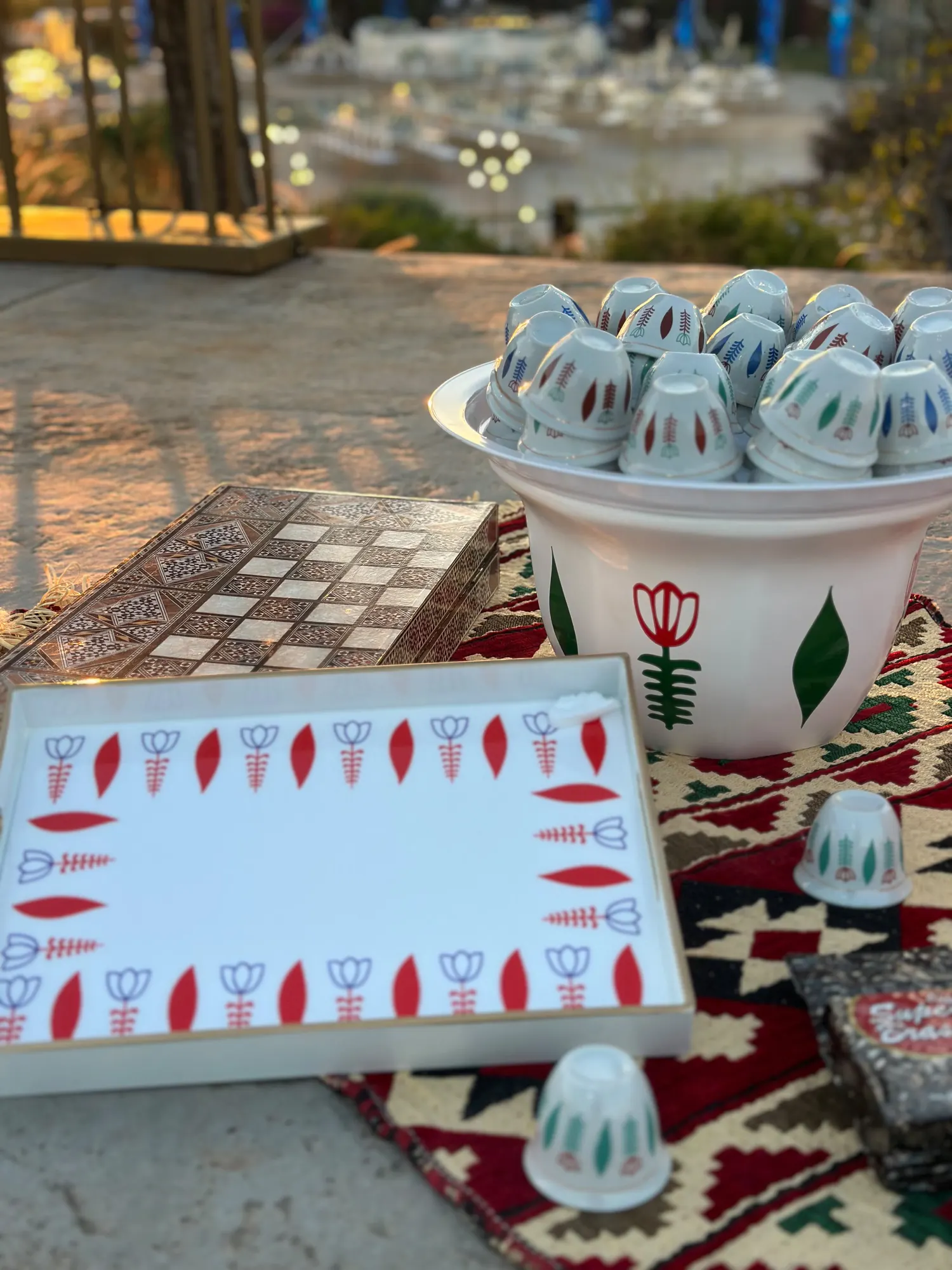 A painted tray and Arabic coffee cups arranged on a woven kilim