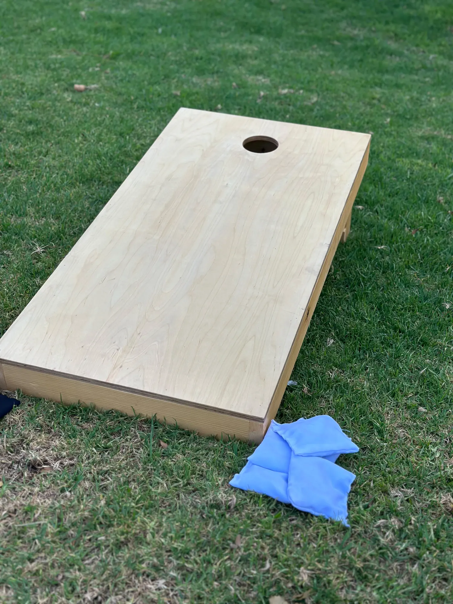 A corn hole board on a lawn with pale blue bean bags