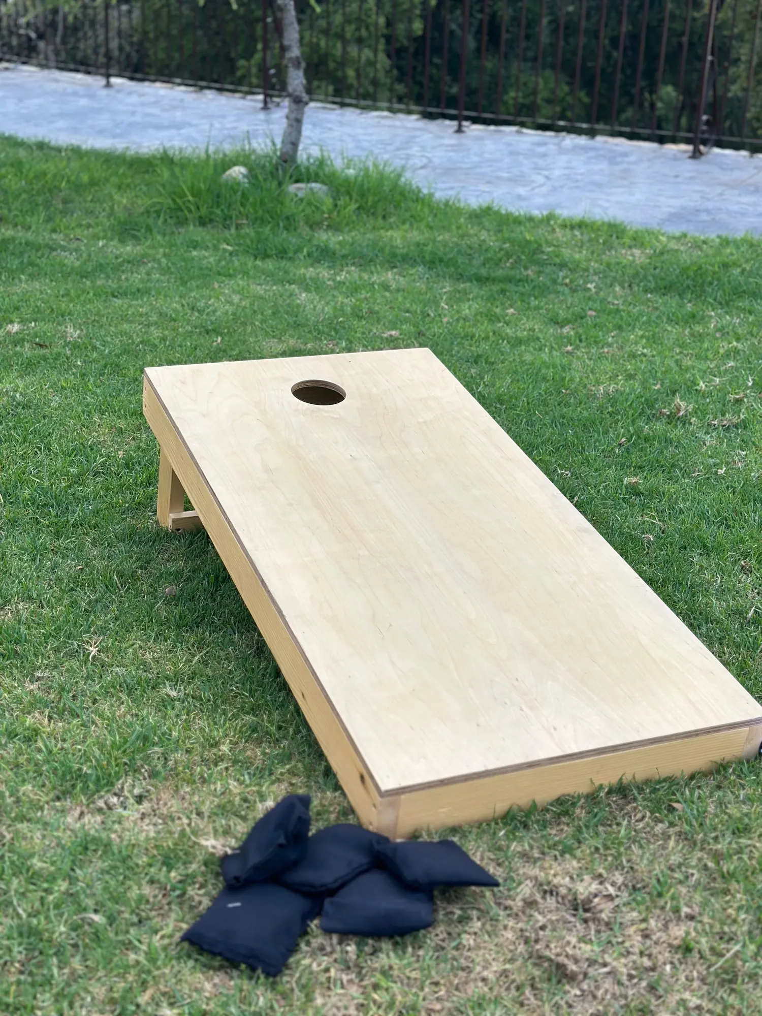 A corn hole board on a lawn with navy bean bags