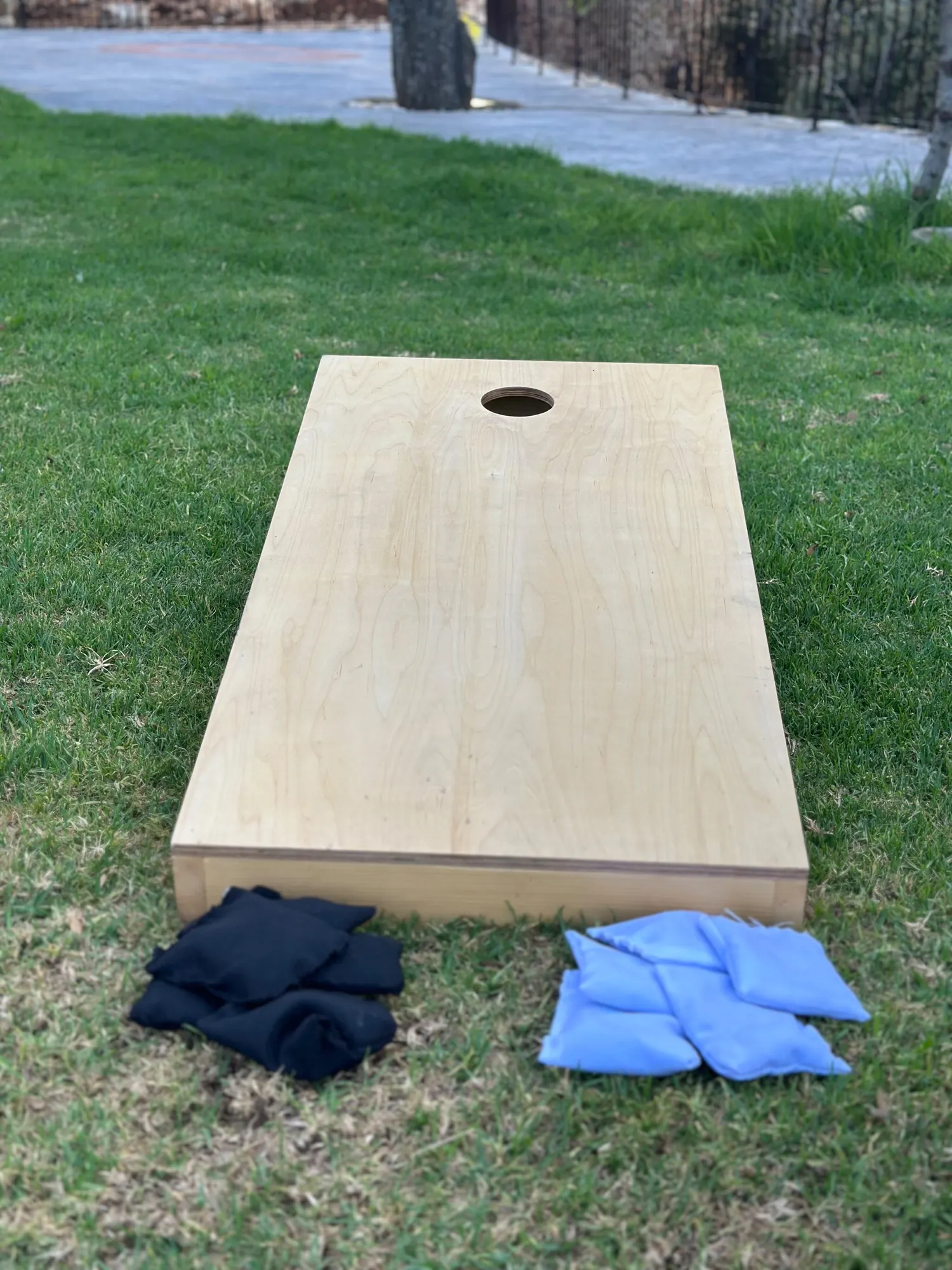 A corn hole board on a lawn with two sets of bean bags