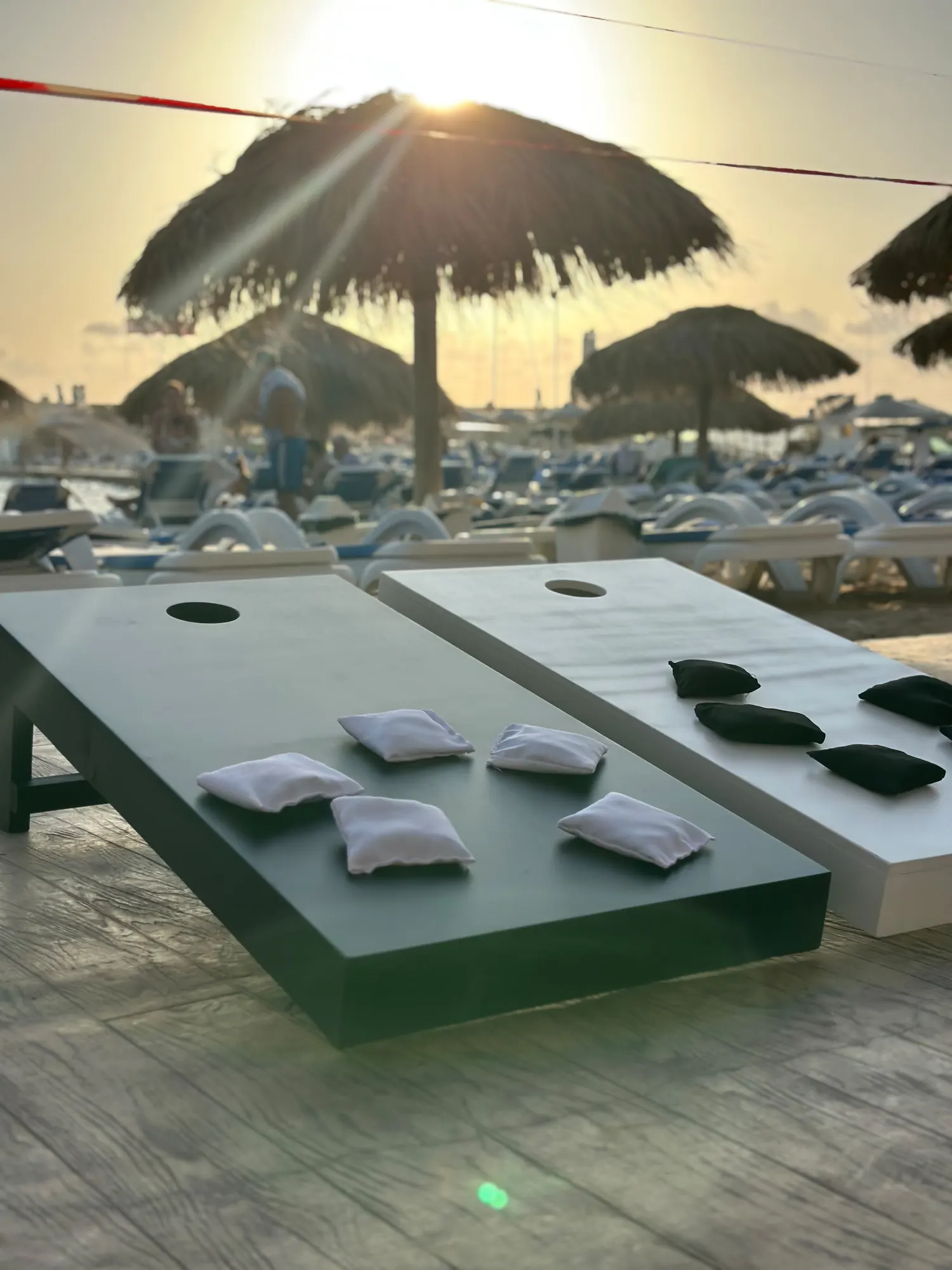 Corn hole boards set up under straw parasols as the sun sets over the sea
