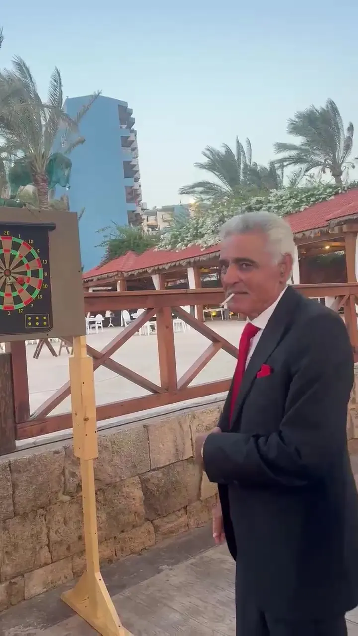 A guest in a tuxedo playing darts at an outdoor event