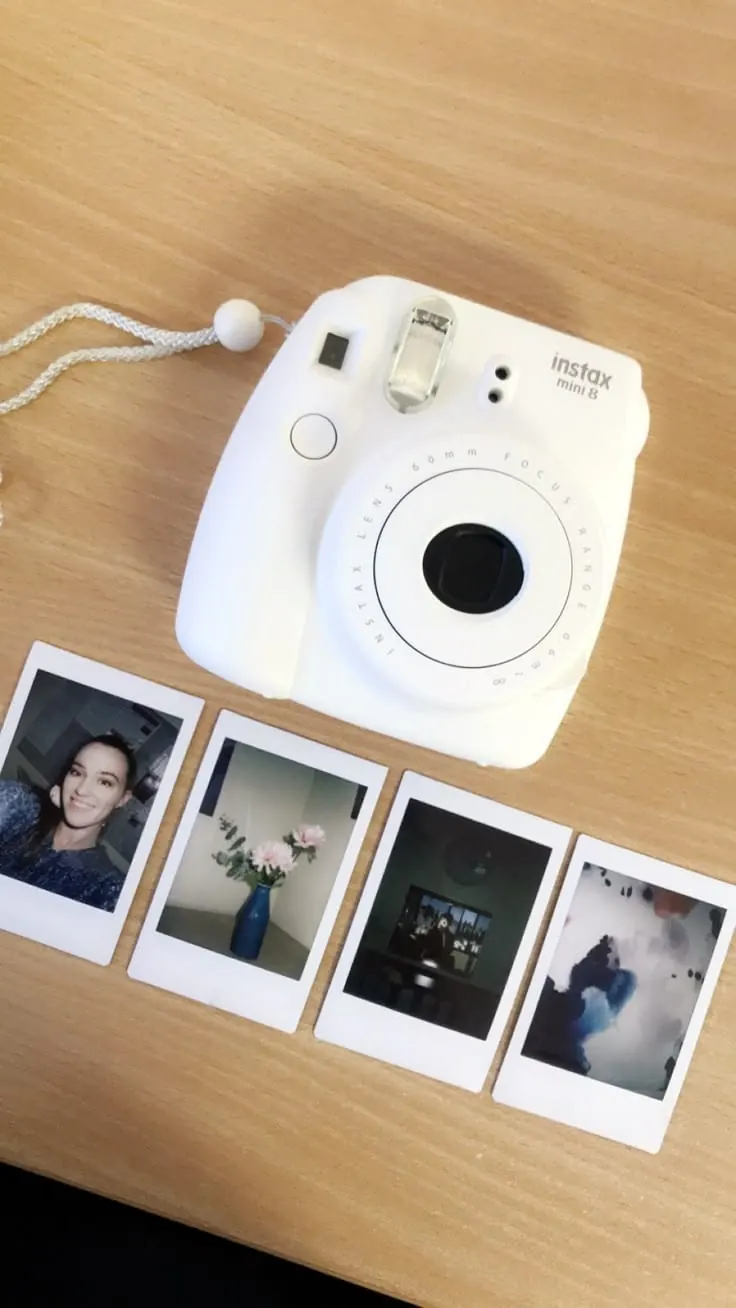 An instant camera on a wooden table beside a row of fresh prints