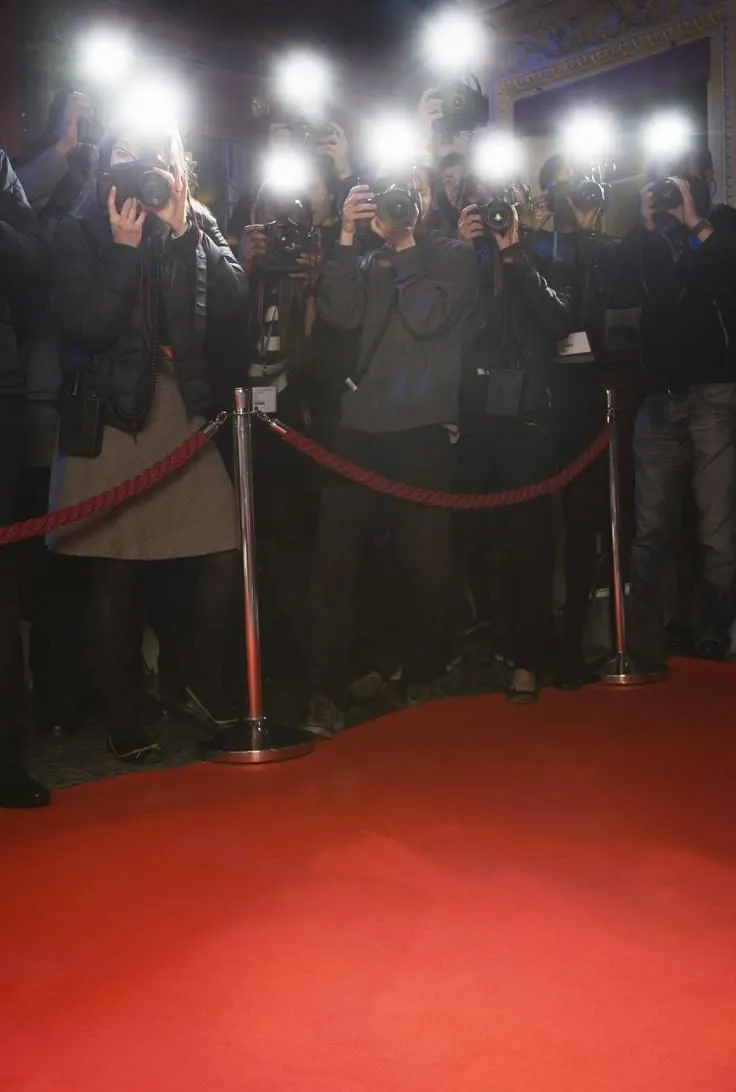 A line of photographers firing flashes behind a rope at a red carpet arrival