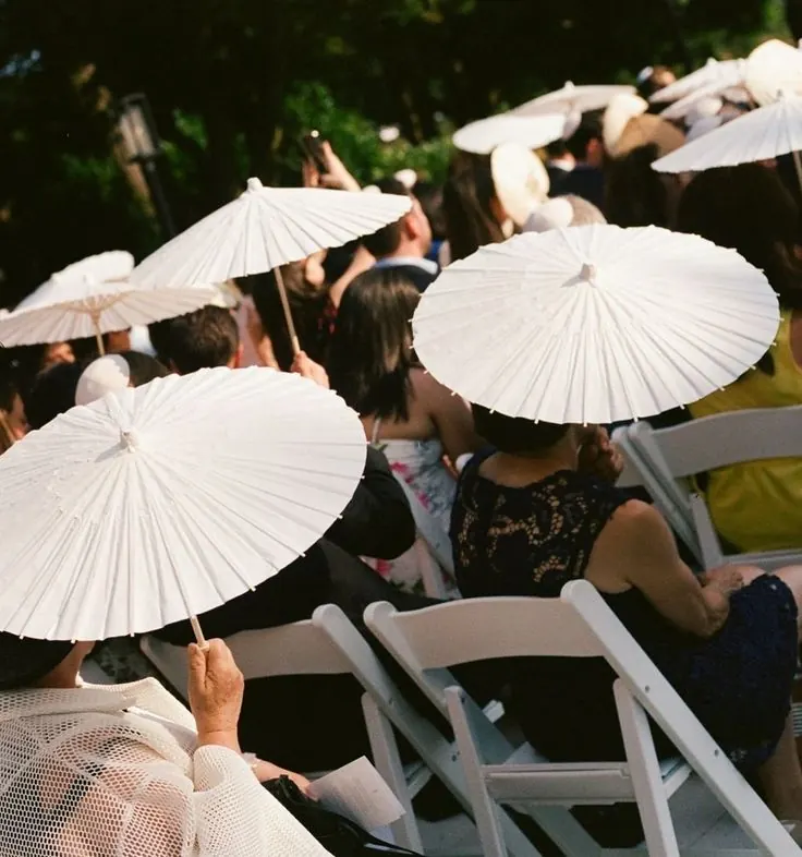 Guests holding white parasols for shade during an outdoor ceremony