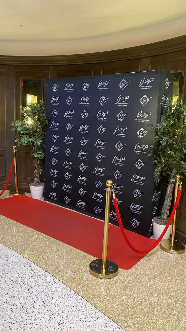 A printed step and repeat backdrop behind a red carpet and rope stanchions
